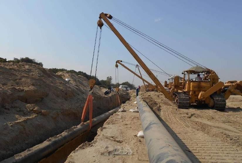 Crane and dozer laying large-diameter pipeline in a desert trench